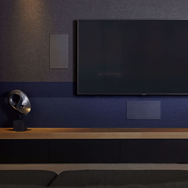 Three speakers embedded in a wall surrounding a TV.